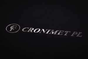 Logotym wykonany w metalu i naklejony na czarny papier